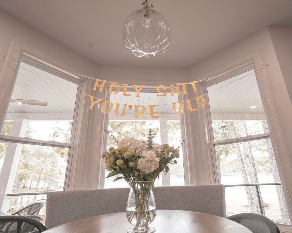 An elegant dining room bay window with sheer curtains and a floral centerpiece under a modern chandelier.