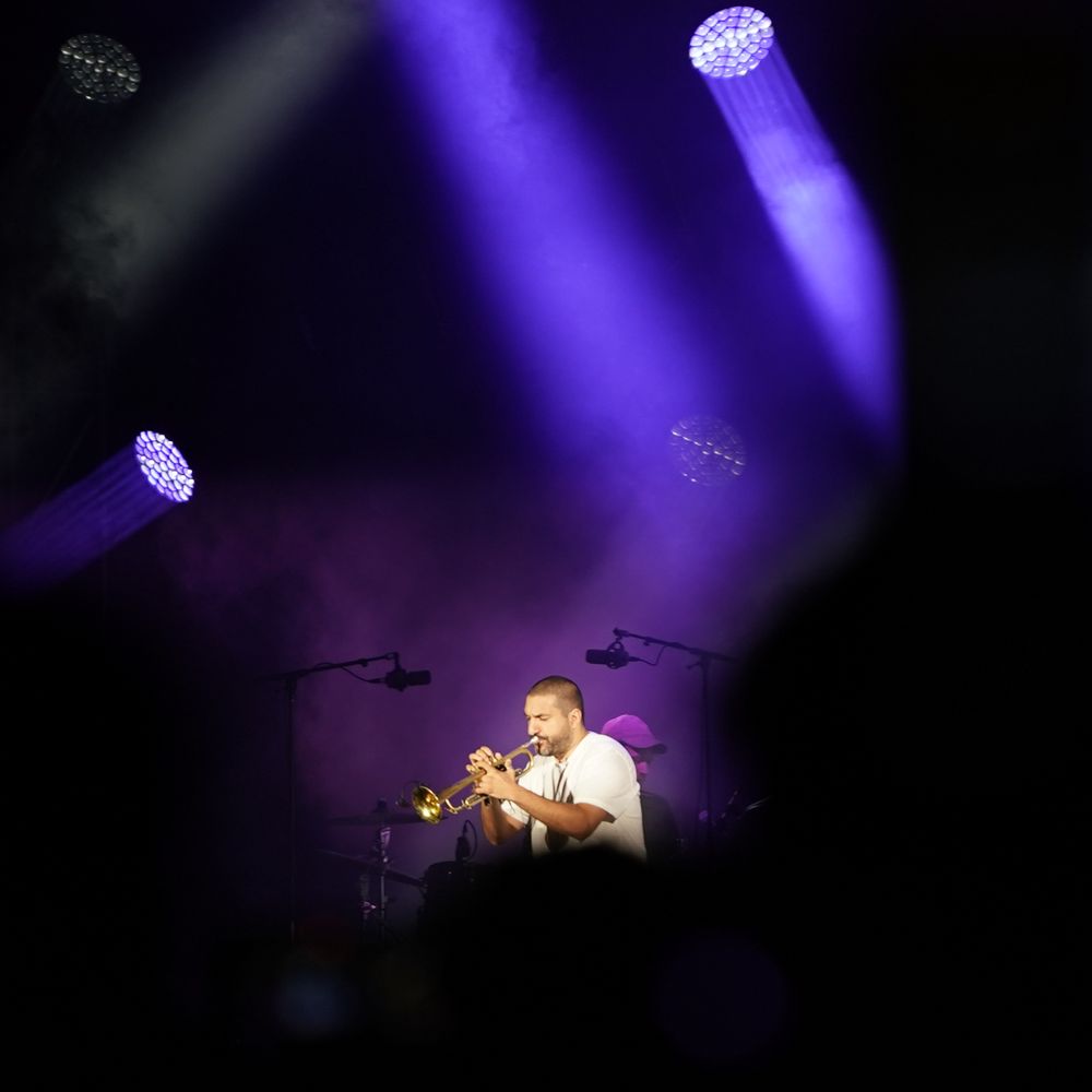 Concert stage with purple spotlights illuminating a performer through a dark atmosphere.
