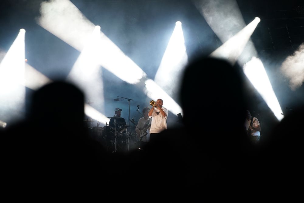Concert performance silhouetted against dramatic white crossing spotlights and fog effects.