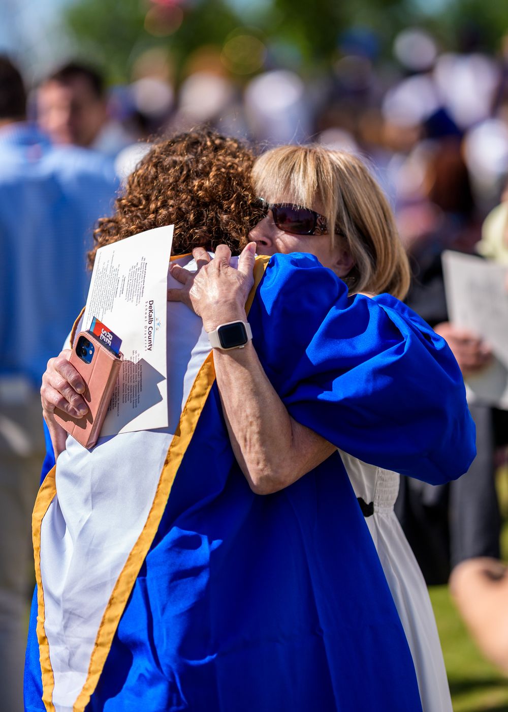 Emotional embrace between graduate and supporter at outdoor graduation ceremony.