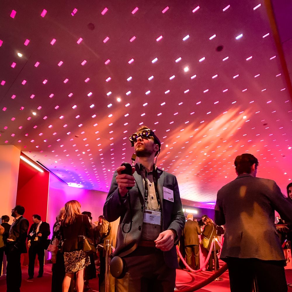 Event space with pink lighting grid ceiling and crowd of people mingling below.