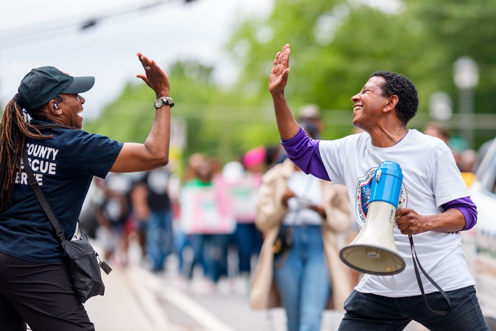 Two people high-fiving with enthusiasm at outdoor event with crowd in background.