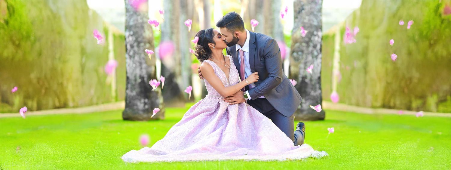 Couple posing romantically on grass with flowering trees in background.