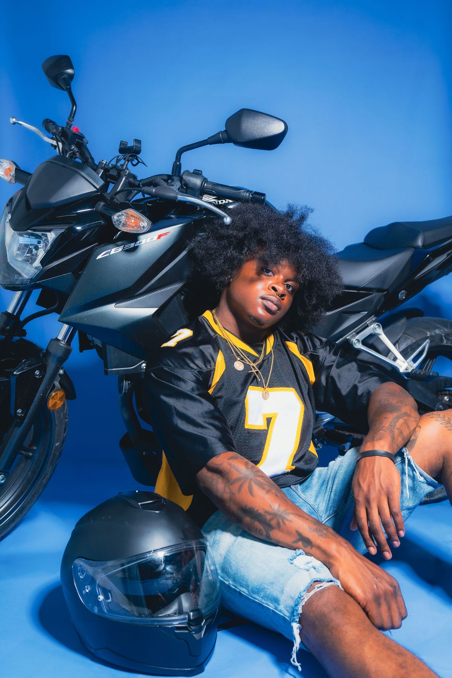 A person in a yellow jersey poses with a motorcycle and helmet against a blue backdrop.