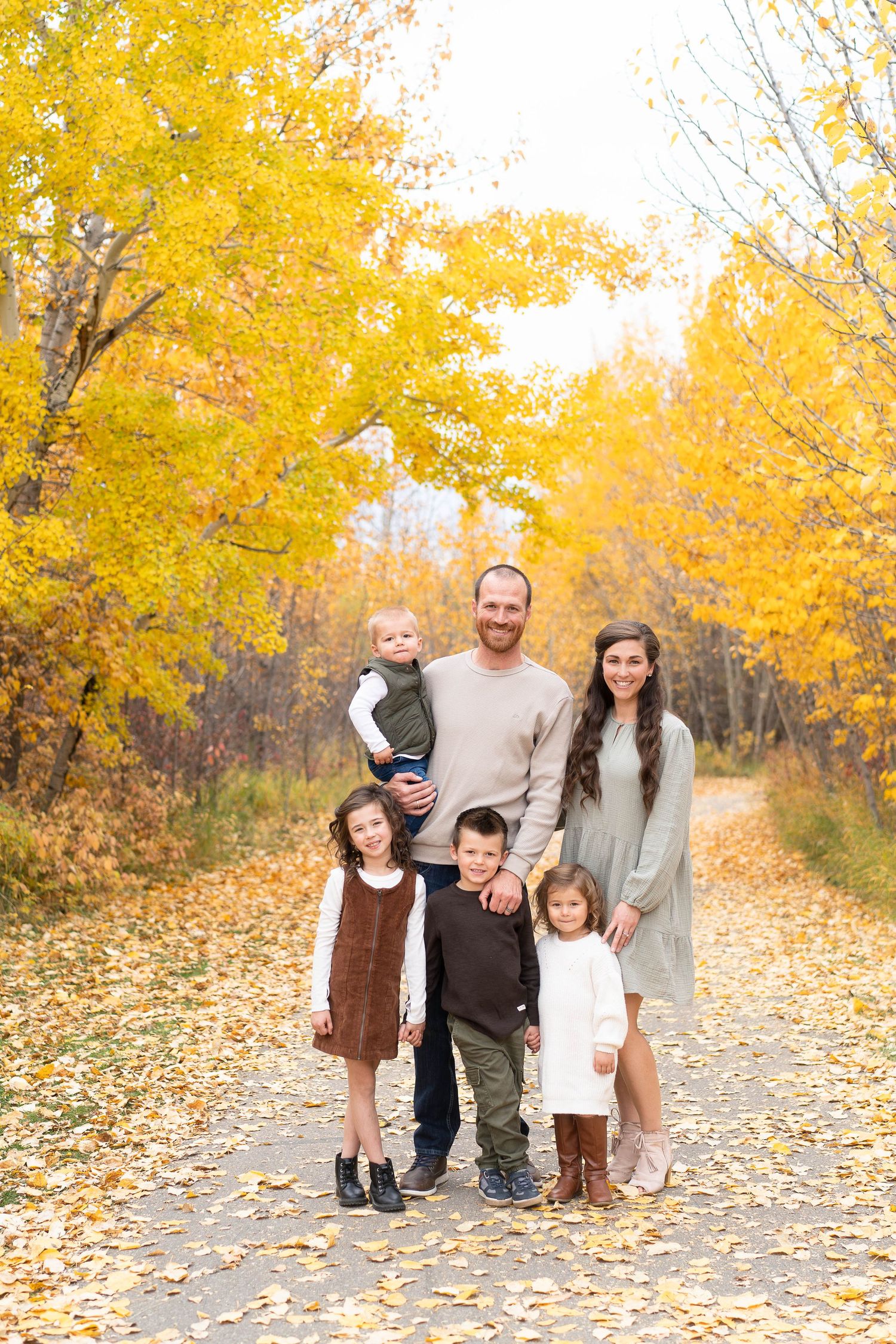 Family portrait on autumn path surrounded by vibrant yellow fall foliage.