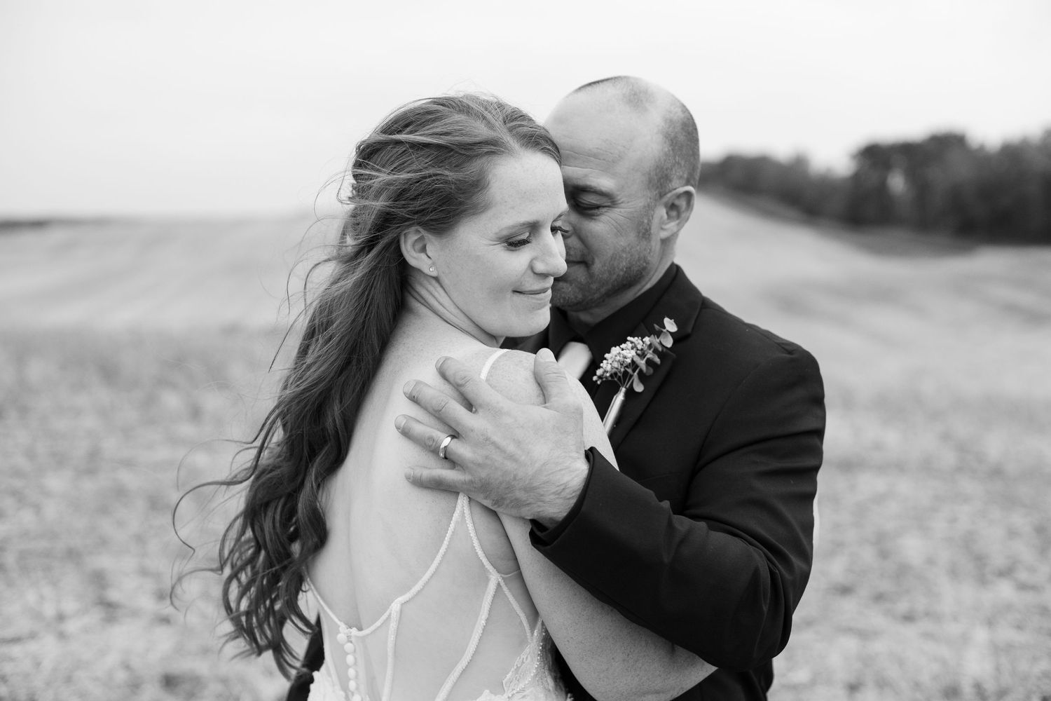 Black and white portrait of intimate wedding moment in open field.