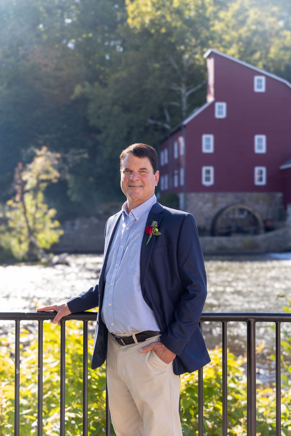 A series of outdoor portraits showing a person in a navy suit and white shirt standing against a railing with a red barn backdrop.