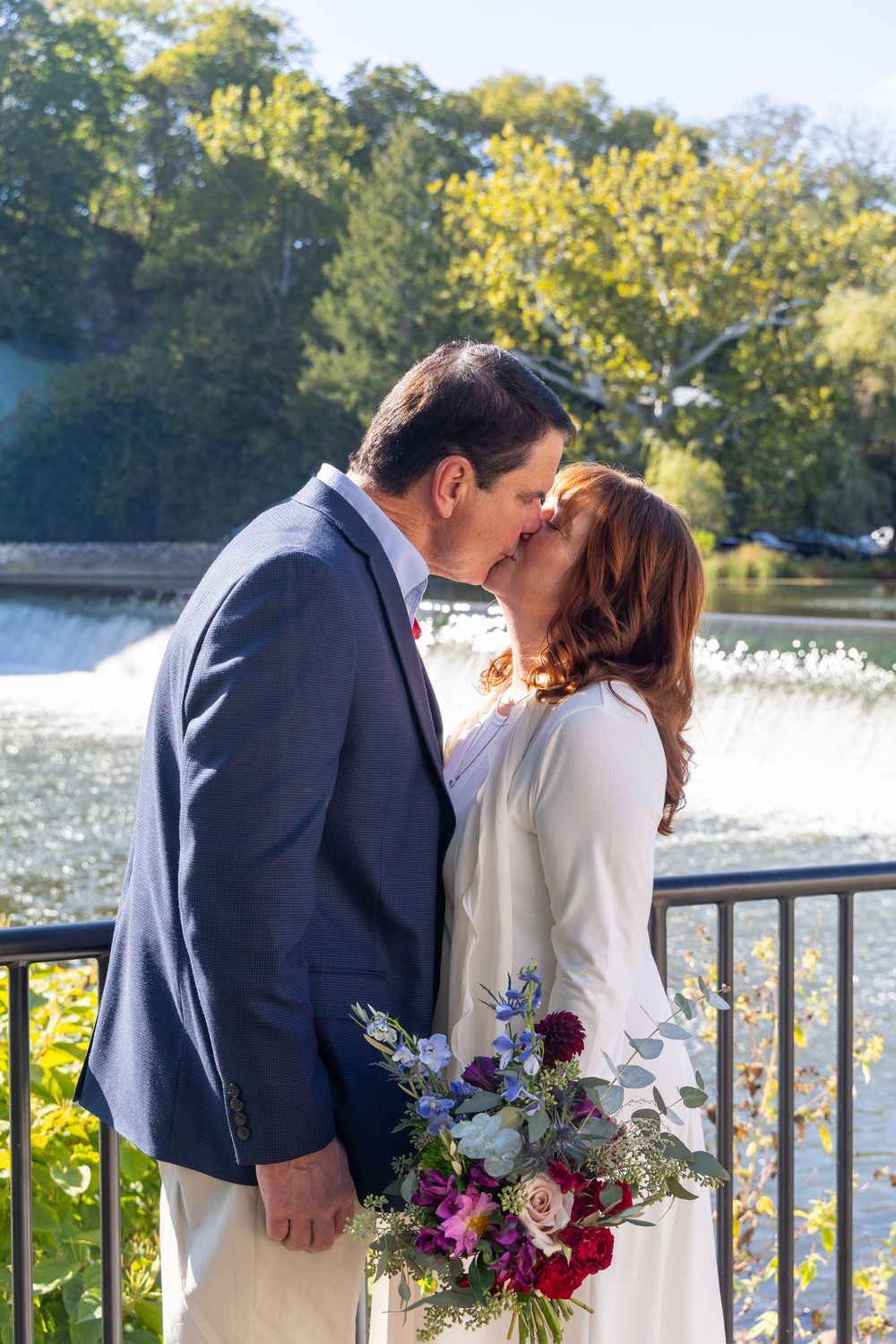 Romantic couple sharing tender moments by a waterfront railing with a colorful floral bouquet.