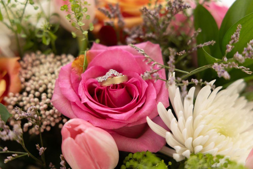 Diamond engagement ring nestled in a pink rose surrounded by a colorful wedding bouquet with tulips and white chrysanthemums.