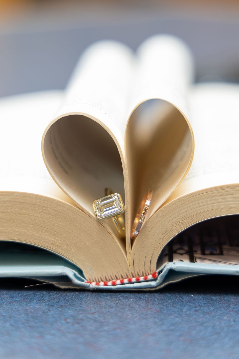 Two gold wedding rings nestled in heart-shaped book pages on a blue surface.