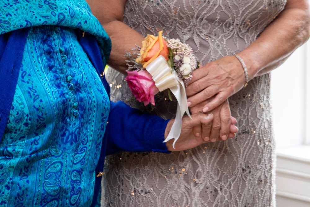 Two elderly women wearing floral wrist corsages at a formal event, dressed in blue and gray lace.