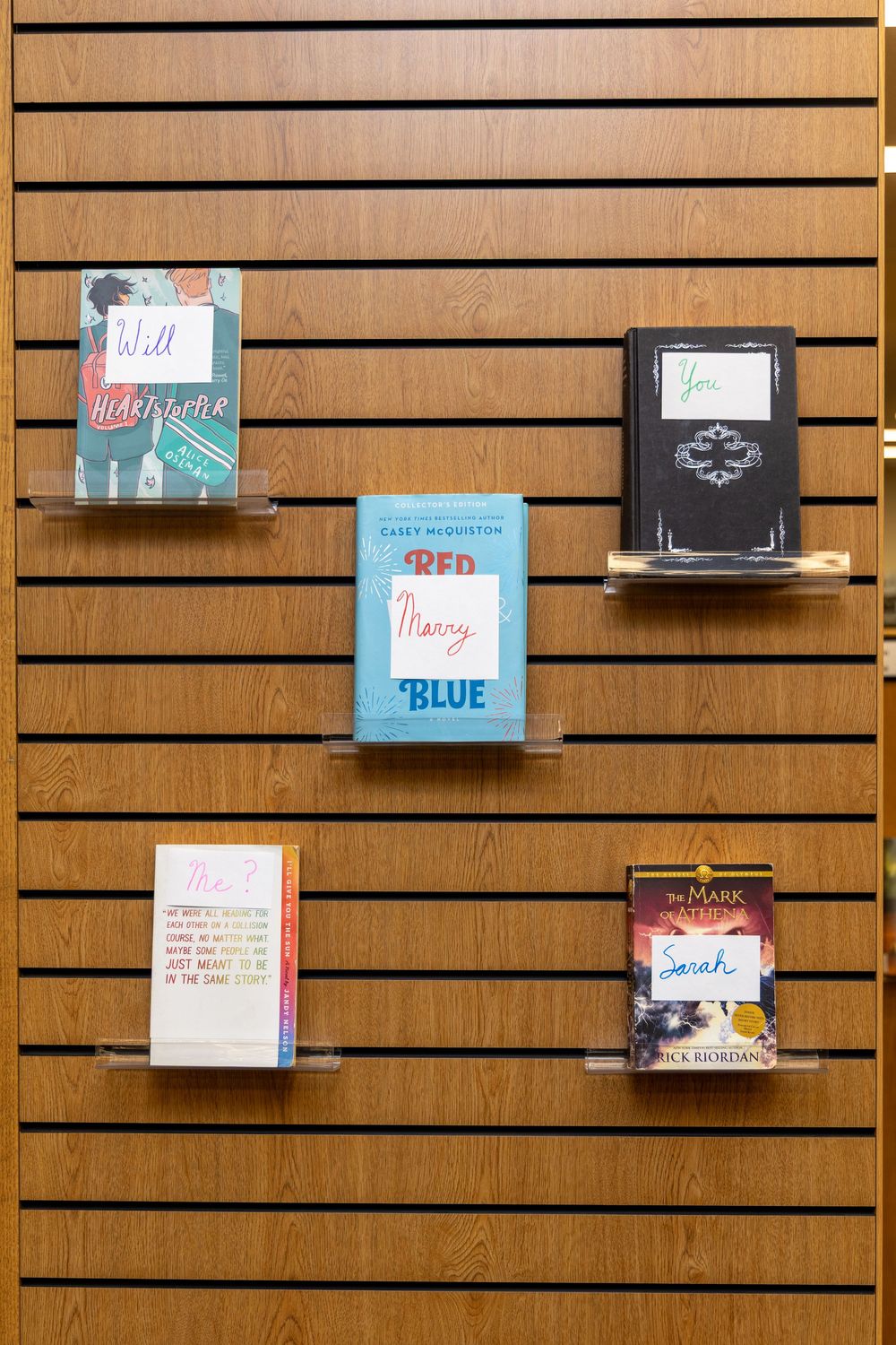 A wooden slatwall display featuring five books including Red White and Royal Blue by Casey McQuiston.
