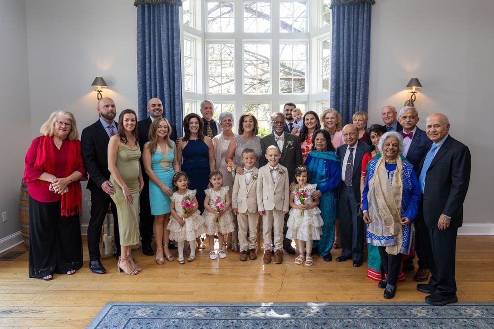 Large family group portrait at a wedding reception, posing together in an elegant blue room with hardwood floors.