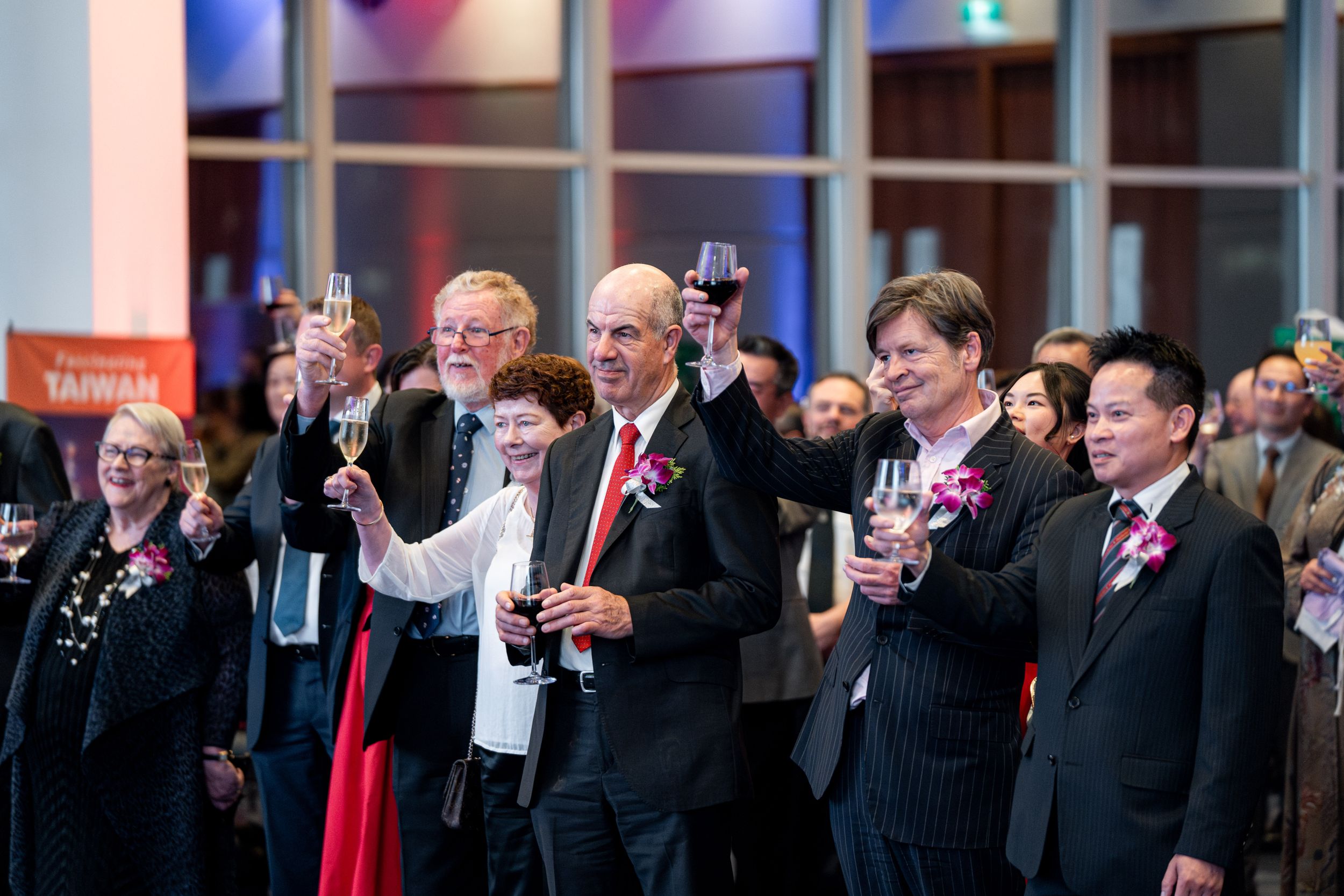 A group of formally dressed attendees raise their glasses in a toast at an indoor event.