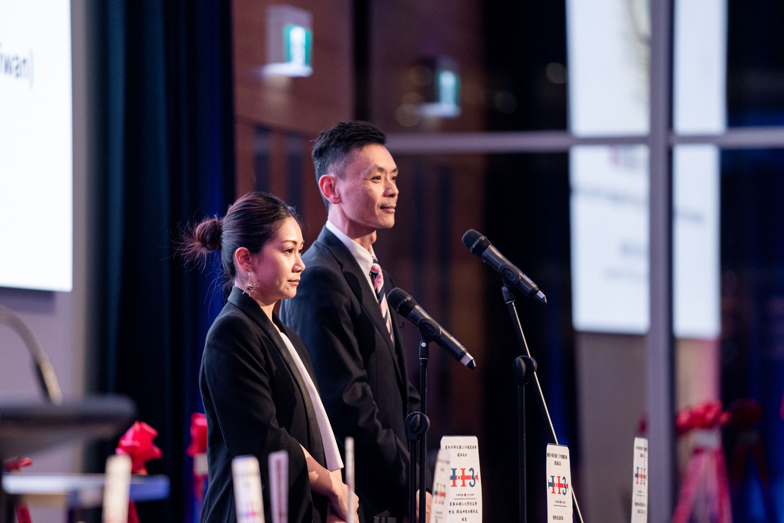 Two speakers at a podium on stage with microphones during a formal event.