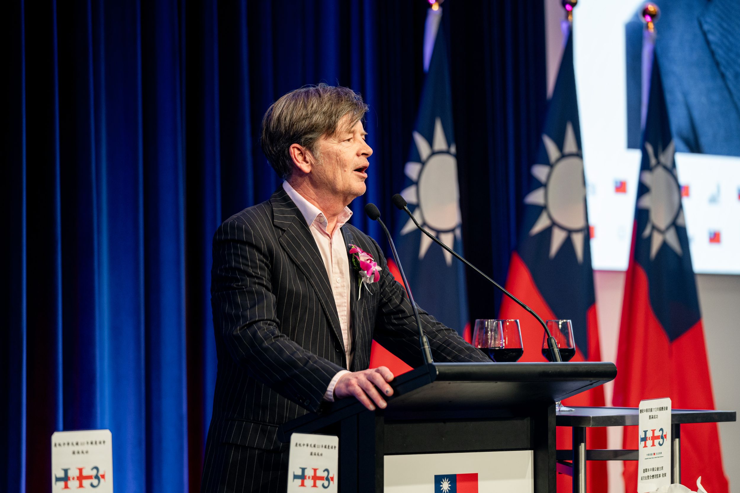 Speaker presenting at podium with multiple Taiwan flags in background.