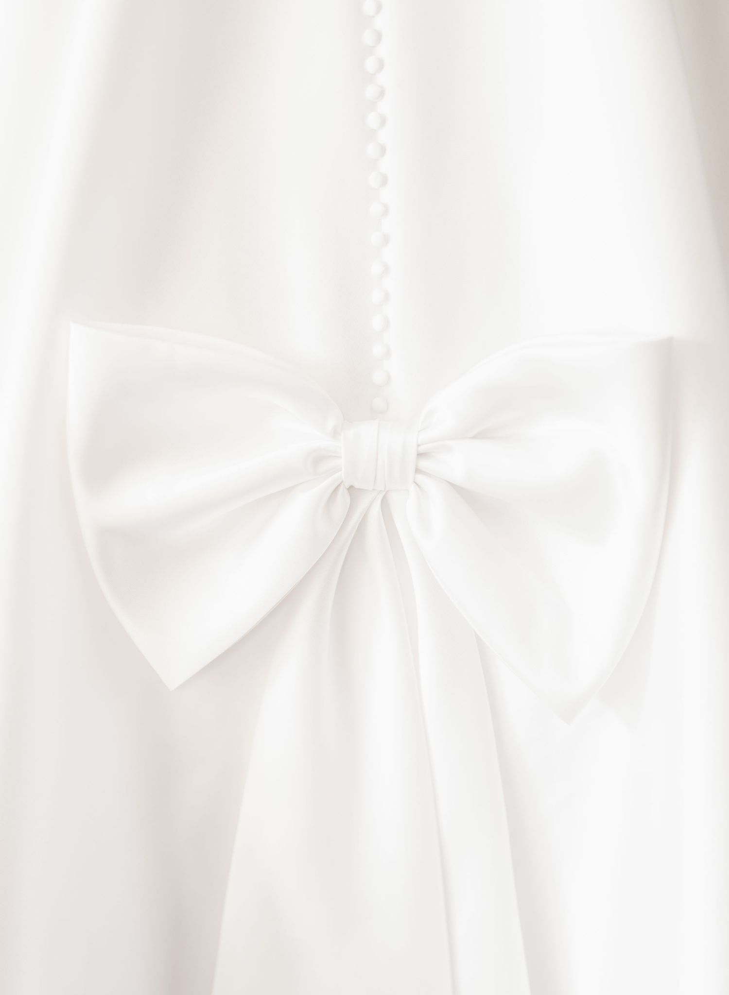 Elegant white satin bow detail on wedding dress fabric.