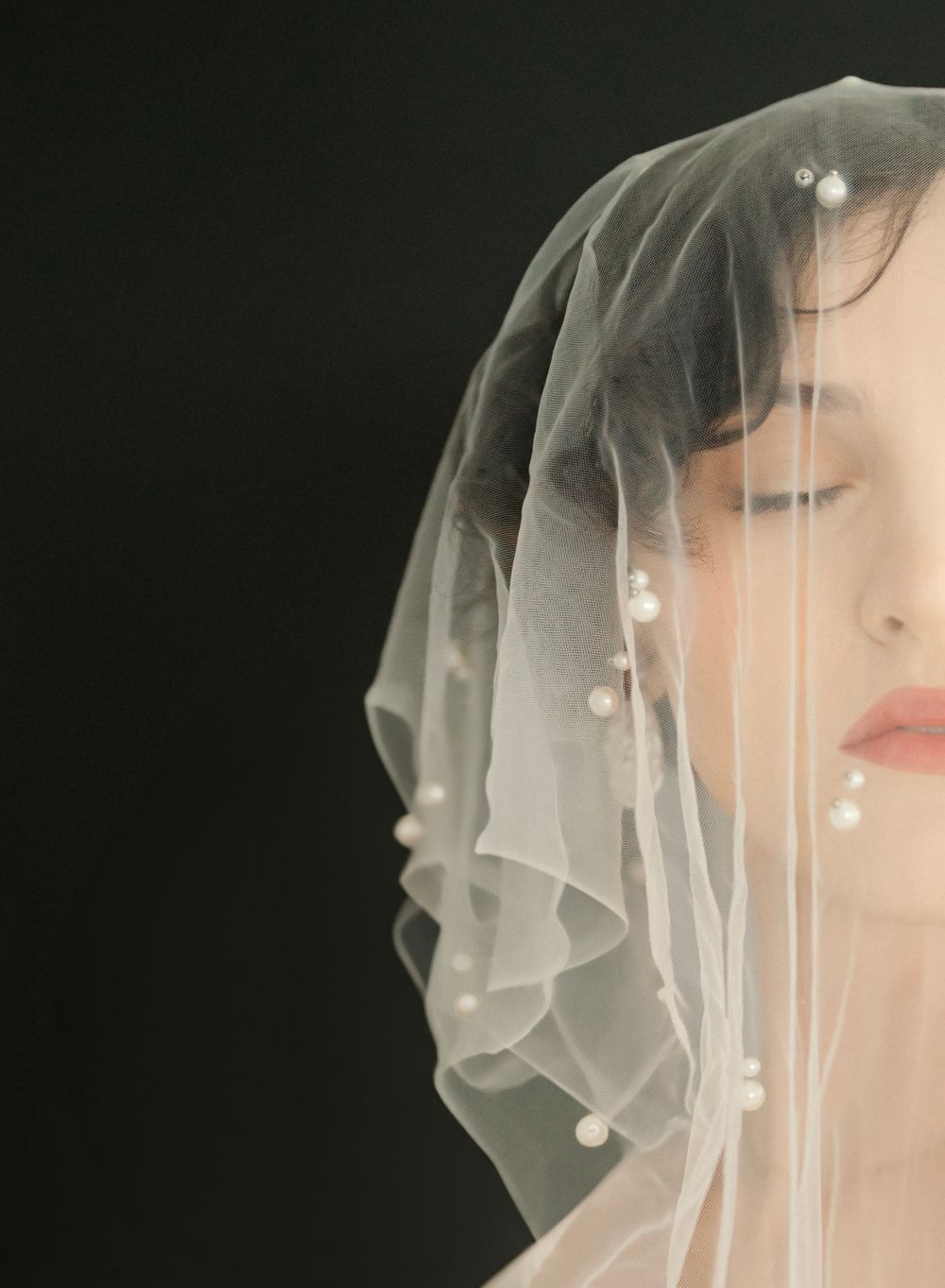 Close-up of a delicate bridal veil with pearl details against a dark background.