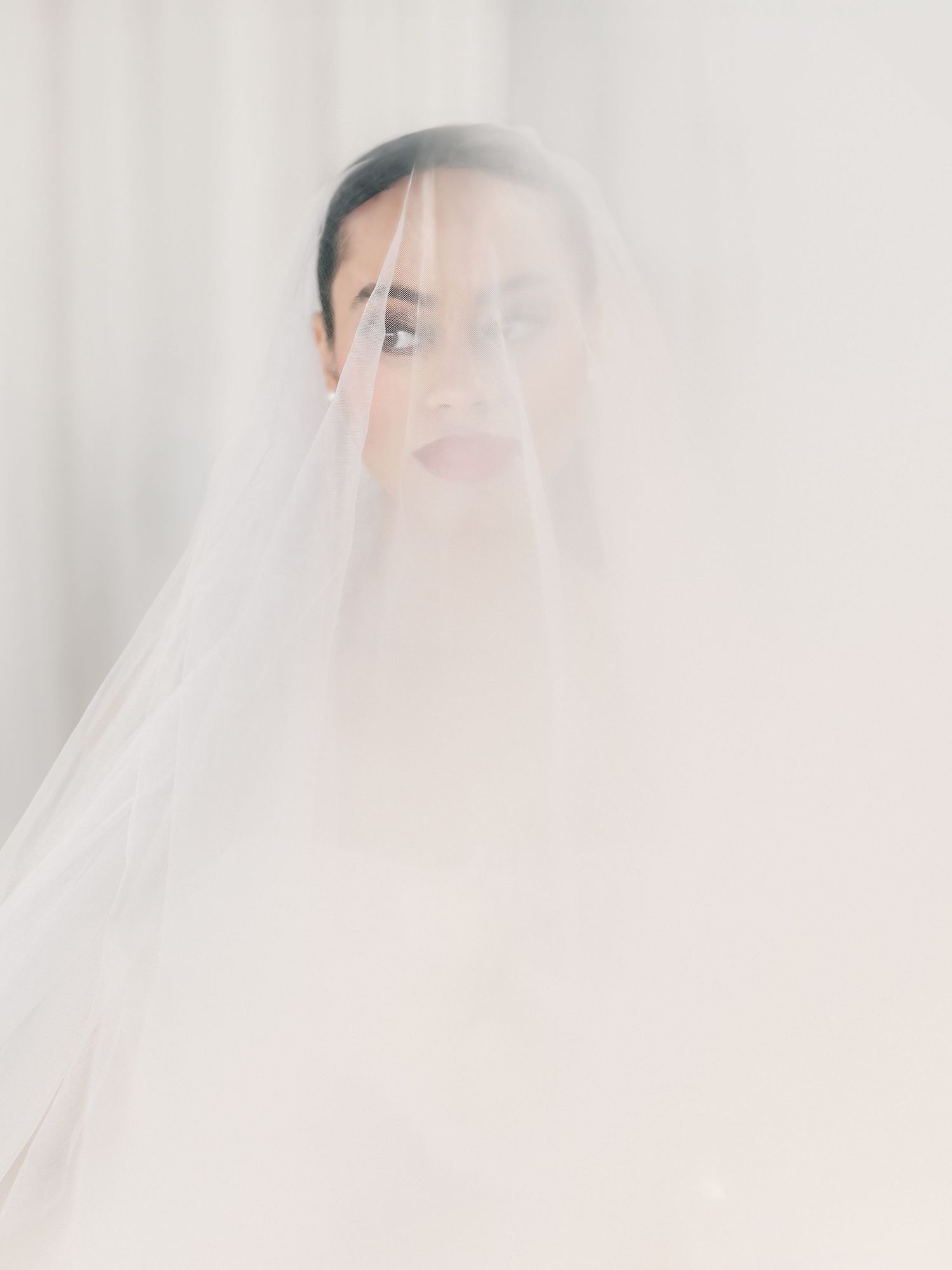Soft focus bridal portrait through sheer white veil creating dreamy effect.