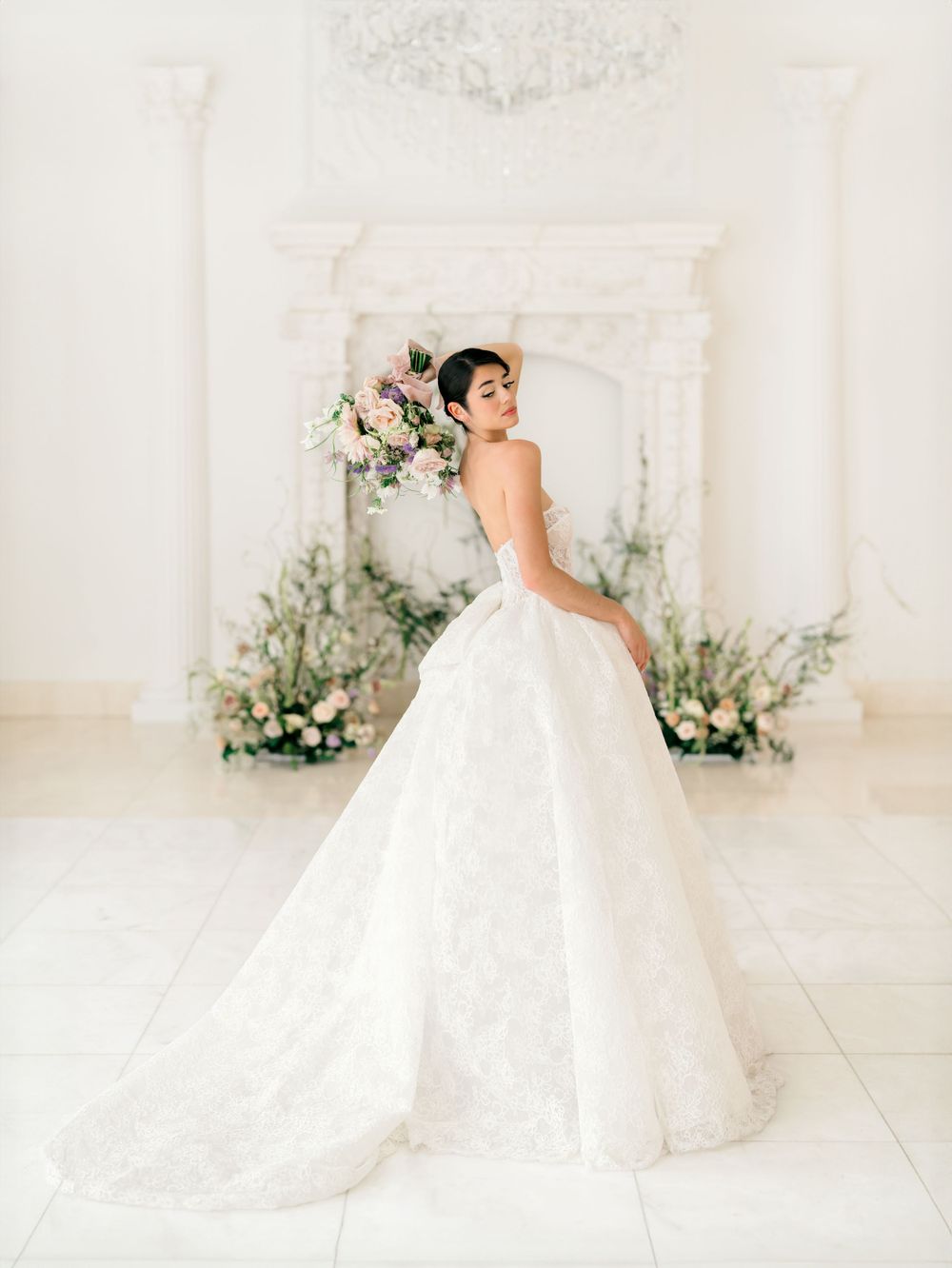 Classic bridal portrait in ballgown against white fireplace decorated with fresh flowers.