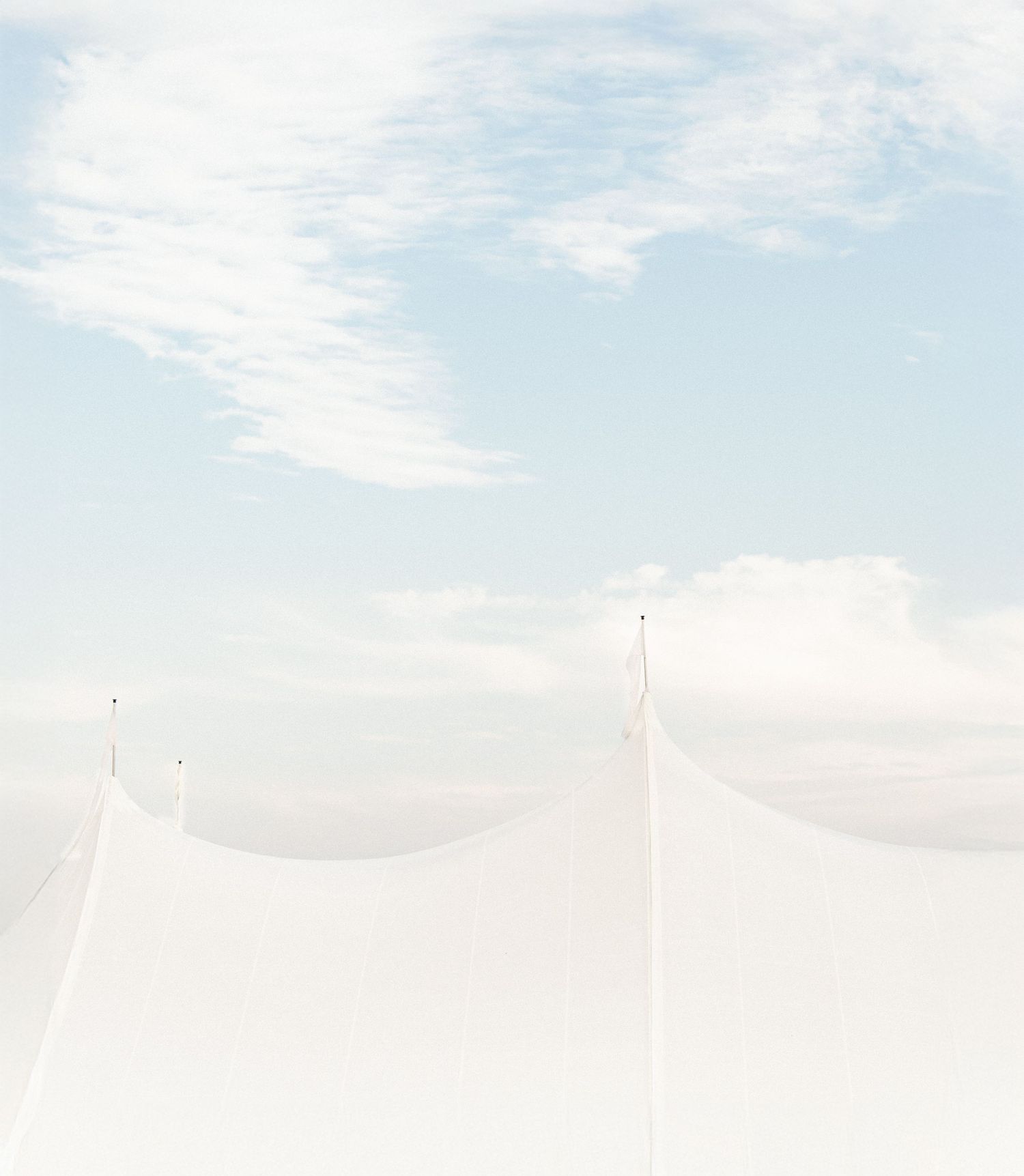 White wedding tent peaks against a soft blue sky with wispy clouds.