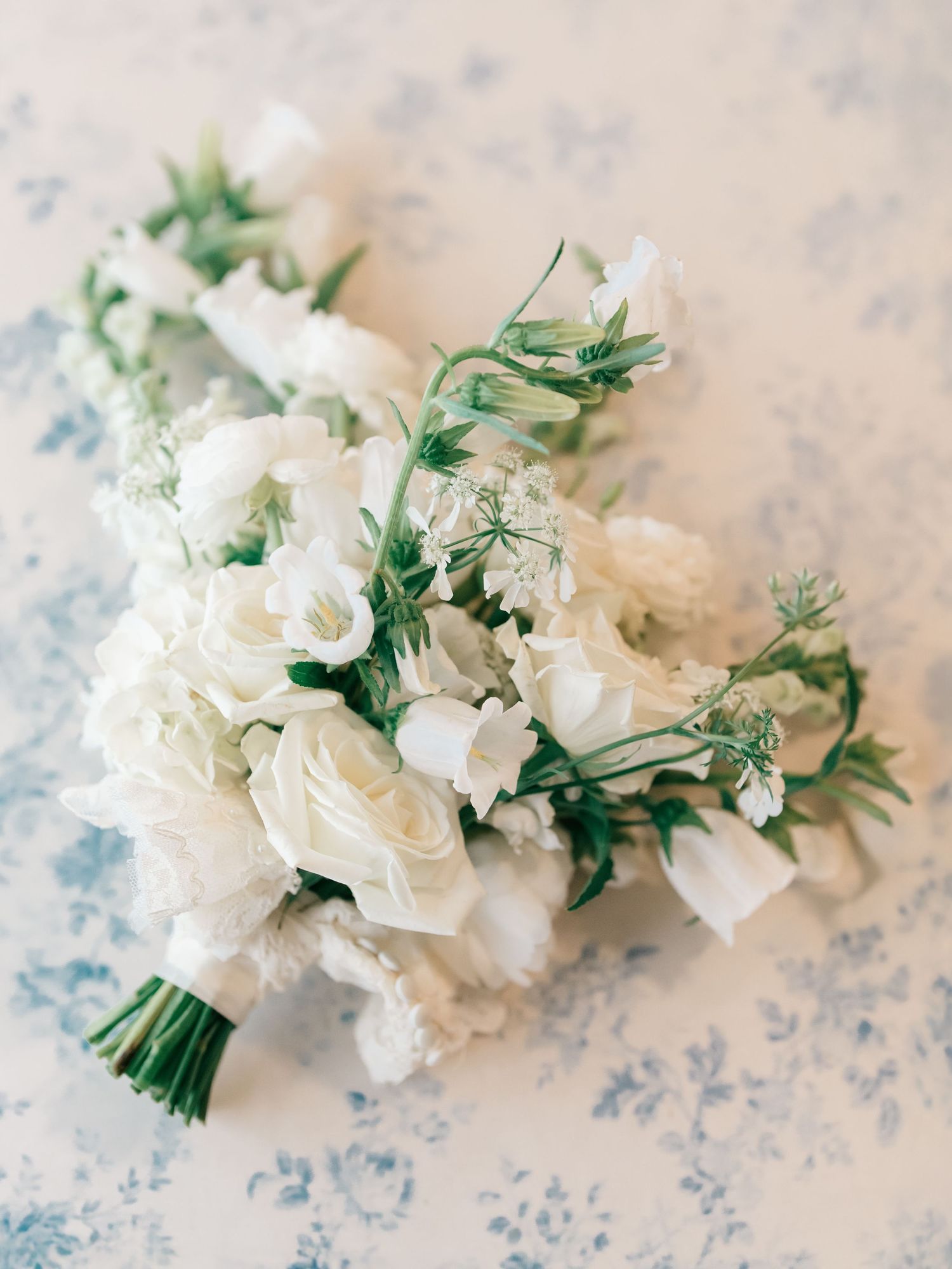 Elegant bridal bouquet of white roses and green foliage arranged with delicate flowing foliage on textured background.