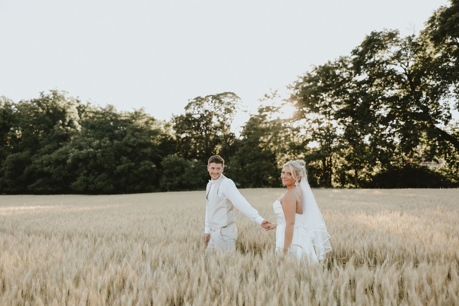 Couple walking hand in hand through golden wheat field at sunset.