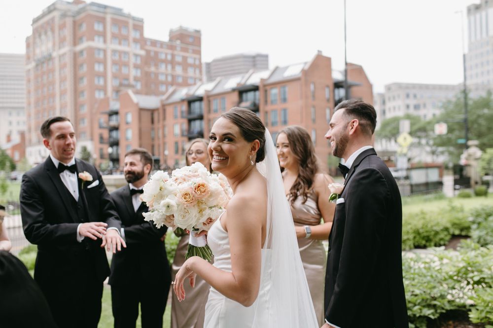 Wedding party gathered outdoors with city buildings in background.