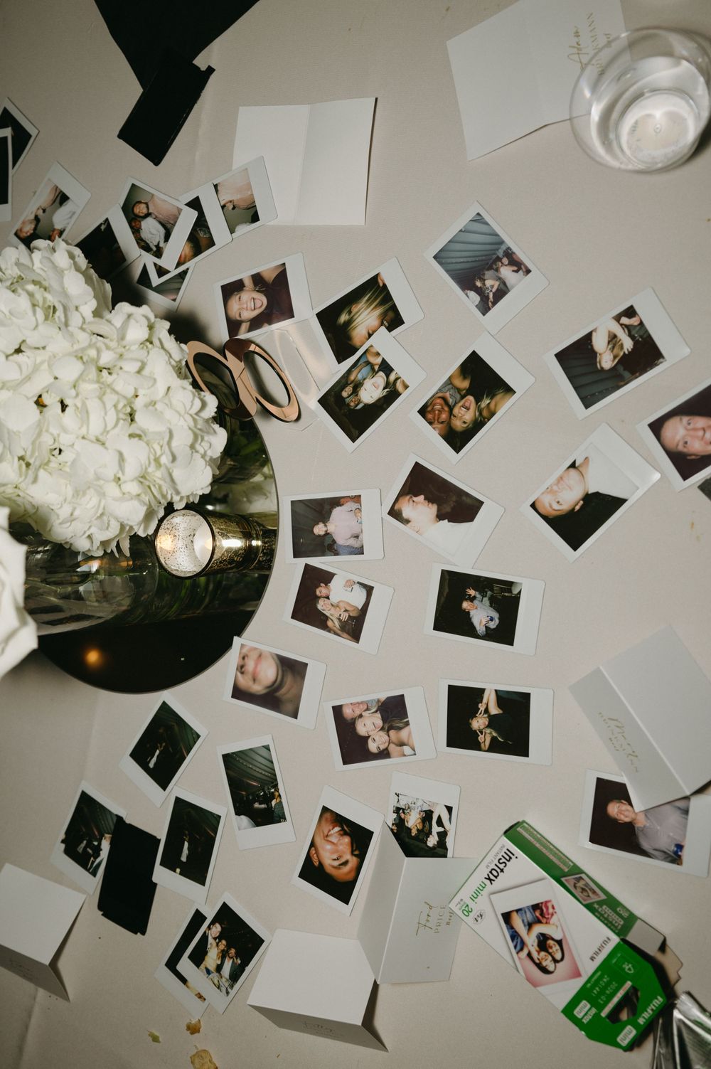Wedding reception detail shot of polaroid photos scattered around white hydrangea centerpiece.