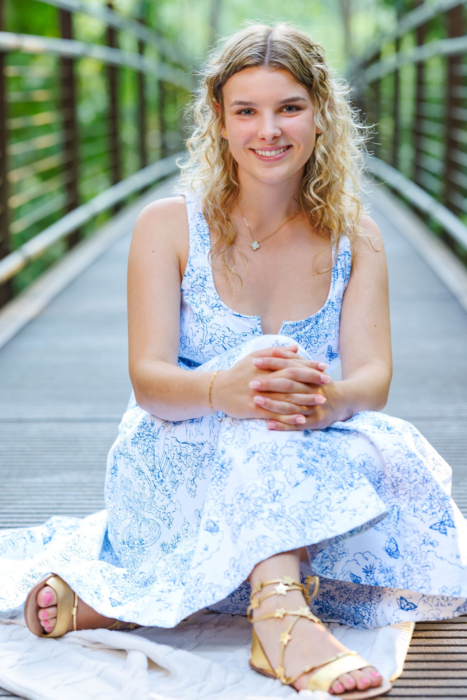 Person in blue floral dress sitting on wooden boardwalk surrounded by greenery.