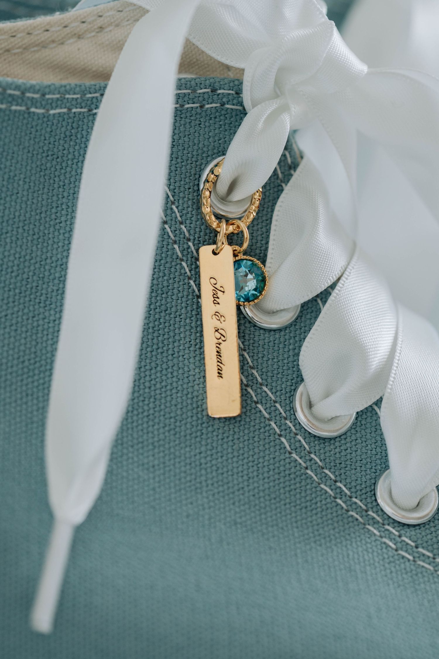 Close-up of turquoise sneaker with white laces and gold charm detail.
