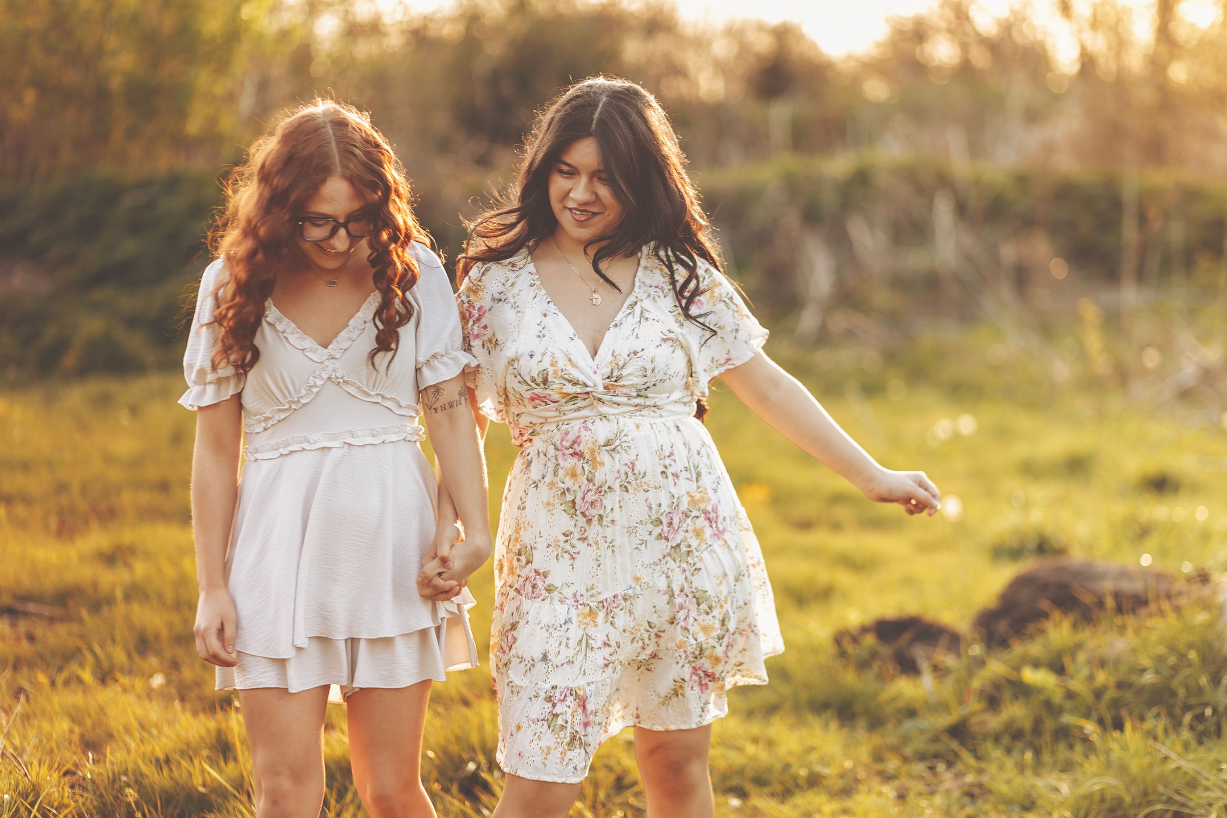 Two friends in summer dresses posing together in a sunlit meadow field.