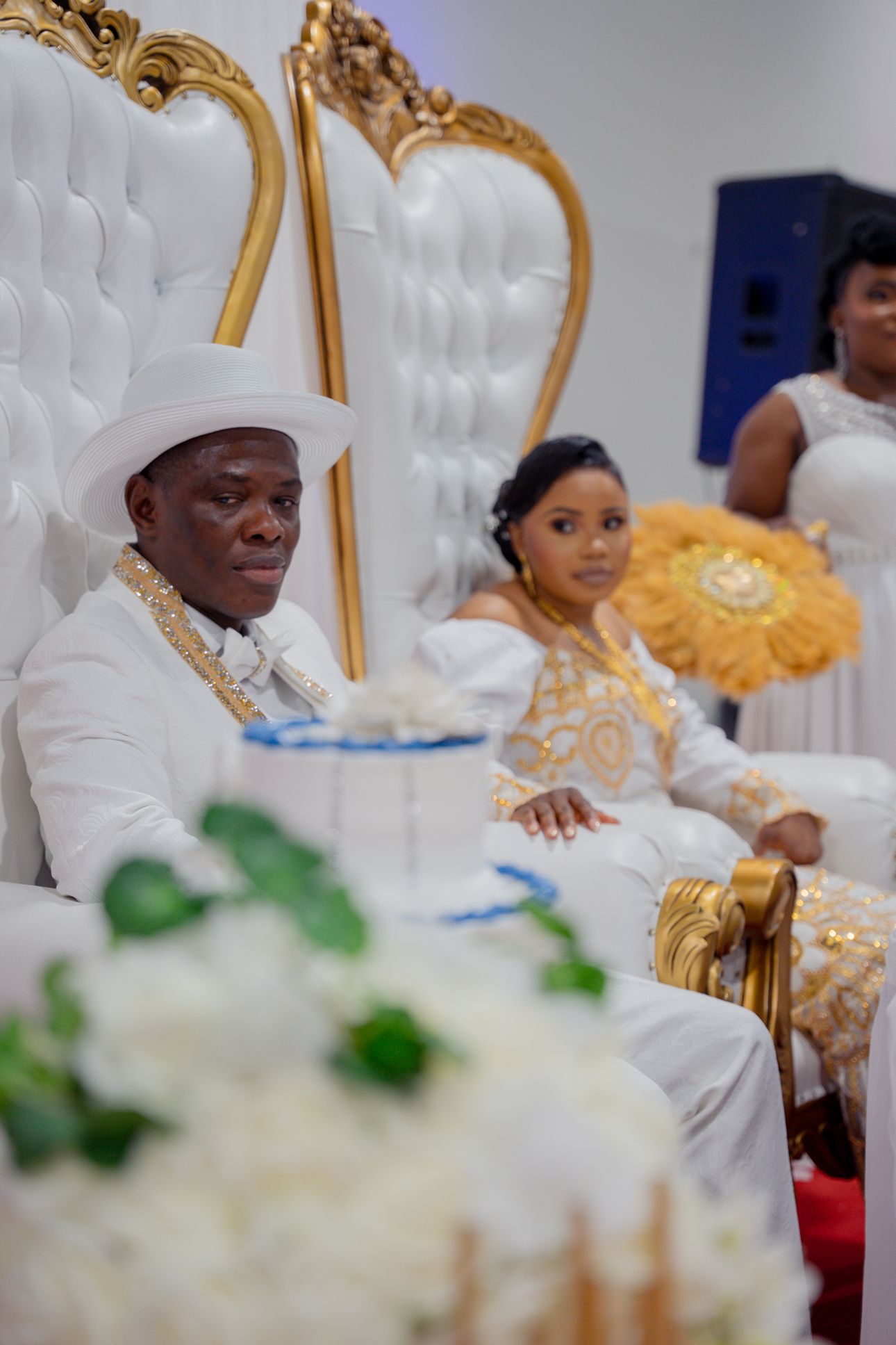 Elegant wedding reception with ornate white and gold throne chairs and floral decorations.