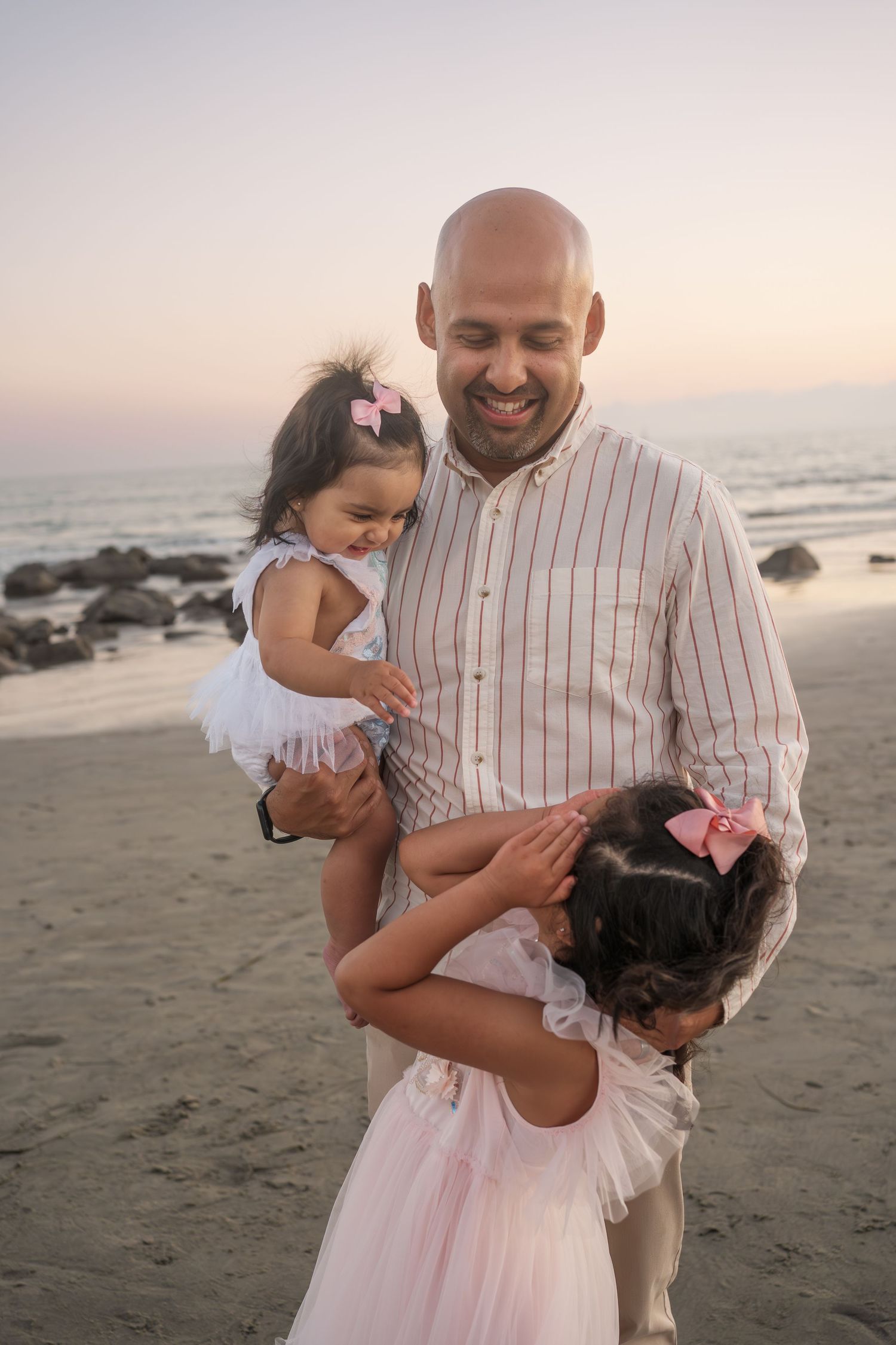 A happy family shares a tender moment together on the beach at sunset against the ocean backdrop.