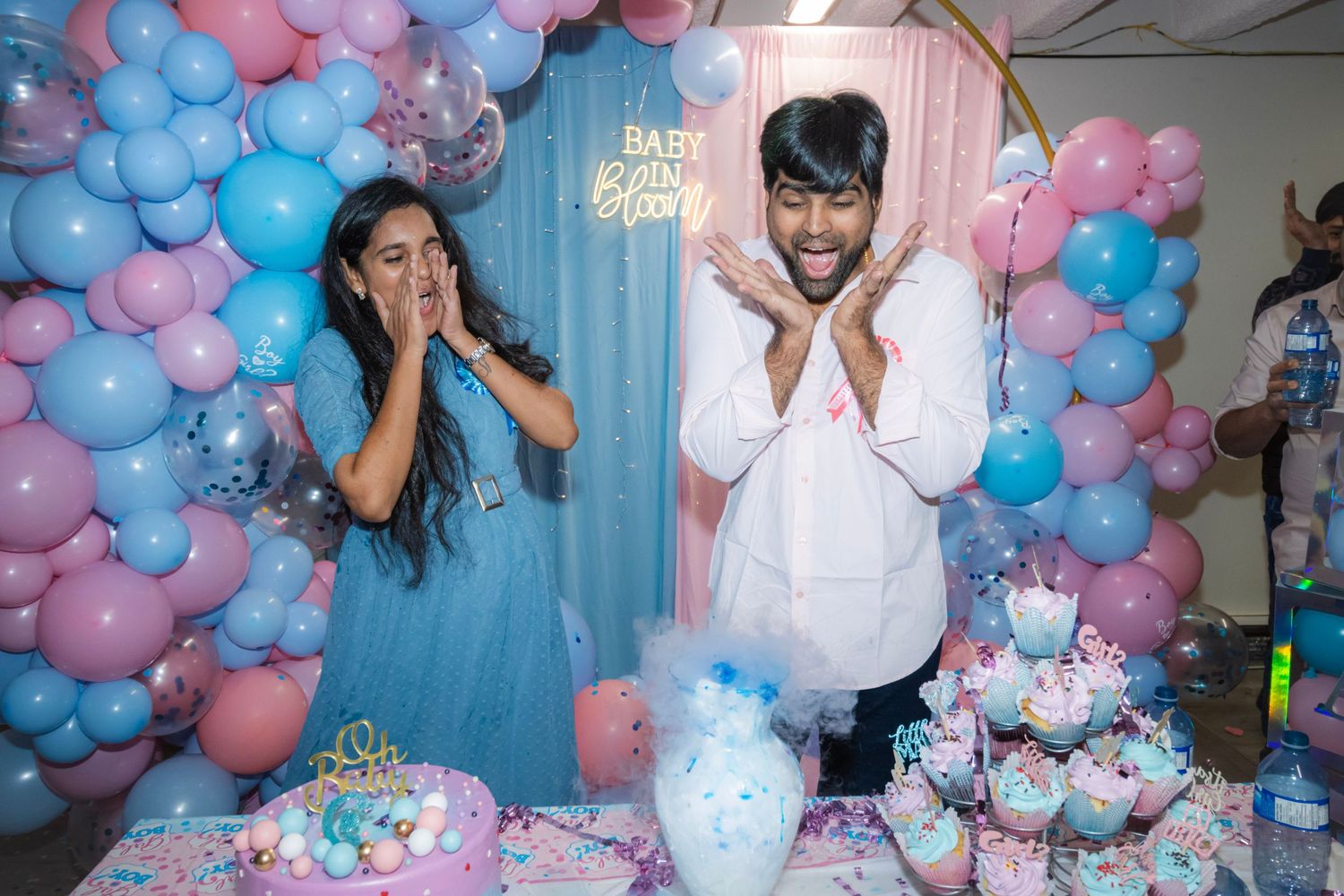 Surprised couple at their gender reveal event with blue and pink balloons in the background