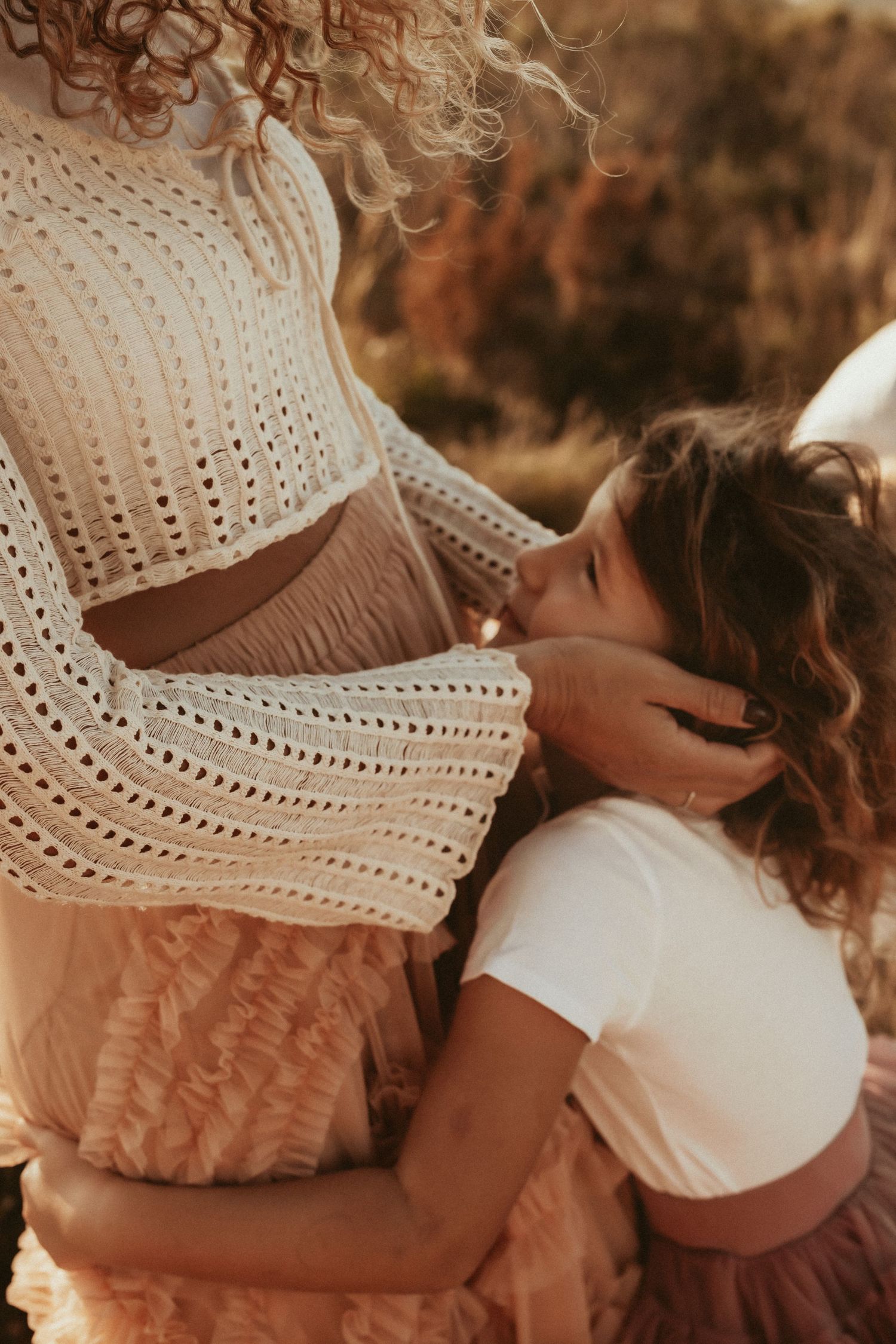 Mom and daughter in Denia share a tender embrace wearing white and dusty pink eyelet lace outfits in warm sunlit setting. Denia photographer