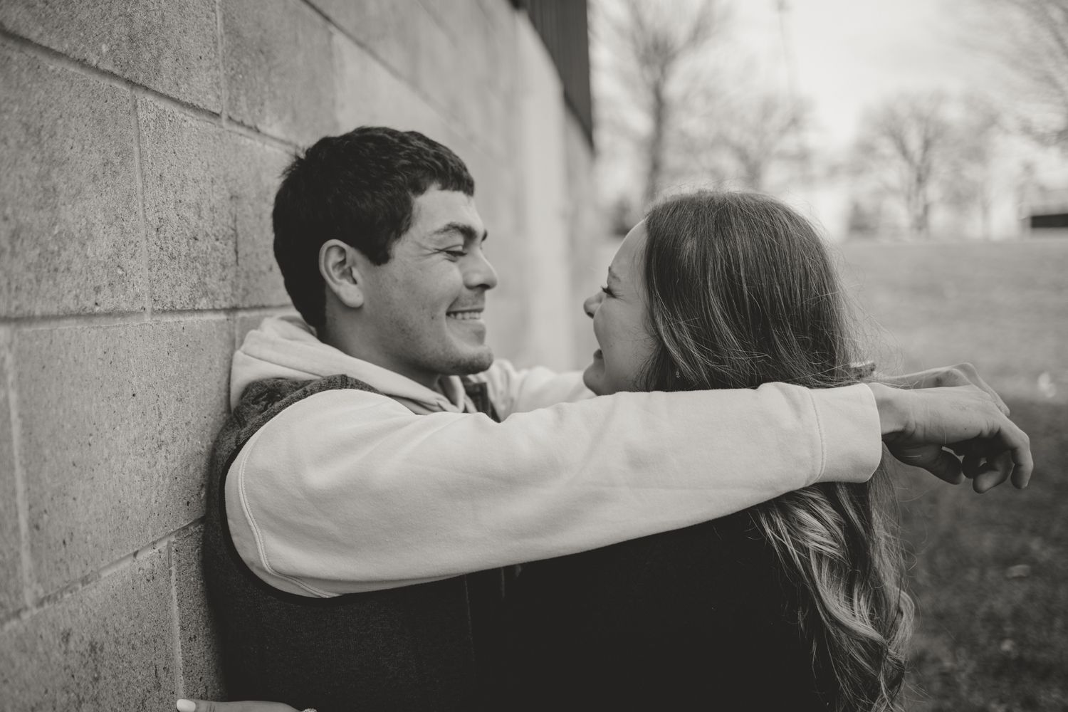 Couple sharing intimate moment against brick wall during black and white portrait session.