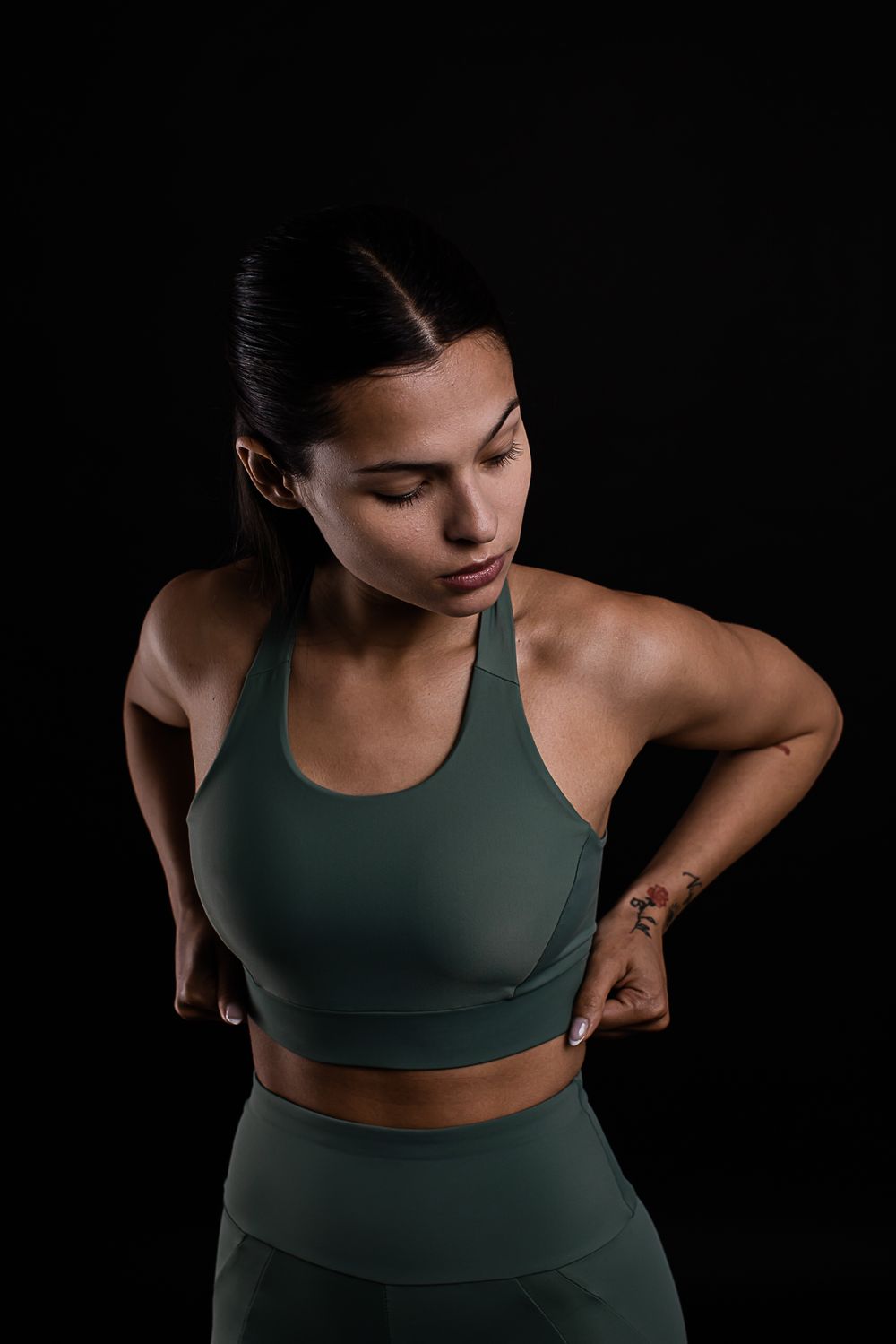Athletic model in olive green sports bra and leggings posing against dark background.