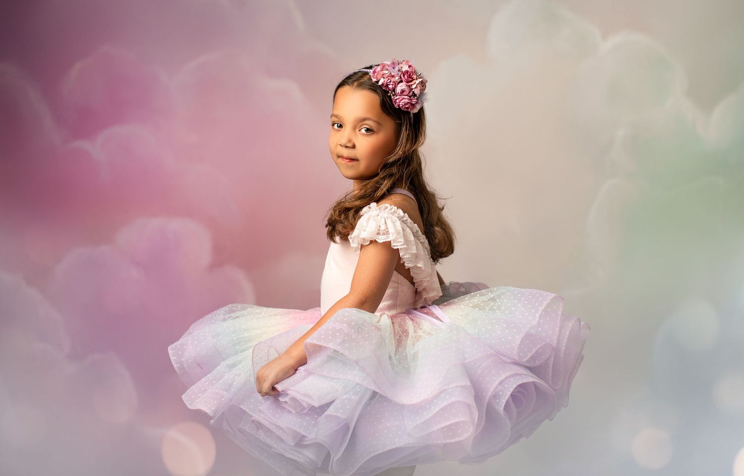 Dreamy portrait in soft pink tulle dress against pastel cloudy background.