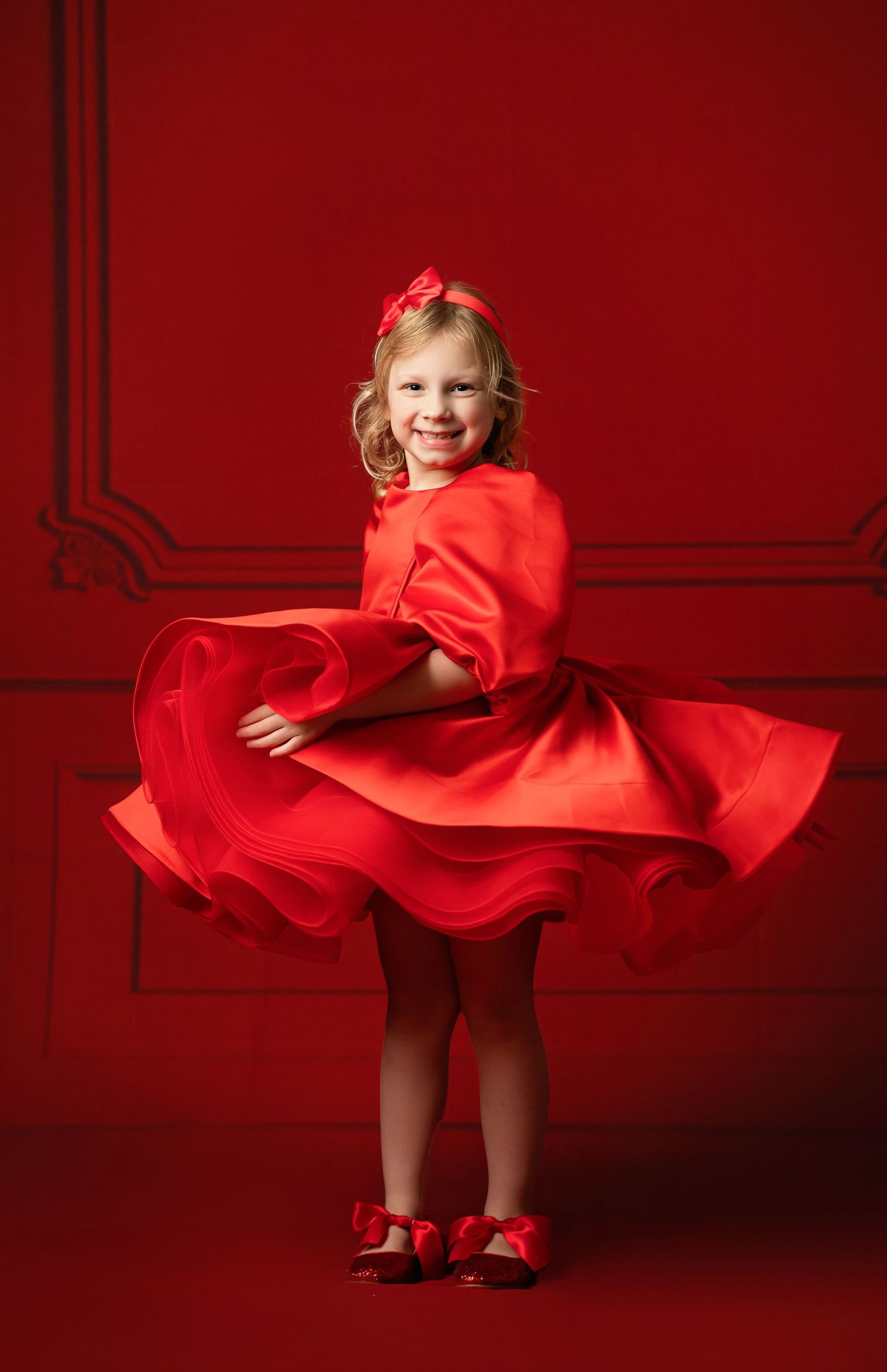 A bright red dress with puff sleeves and heart balloon photographed against a red studio backdrop.