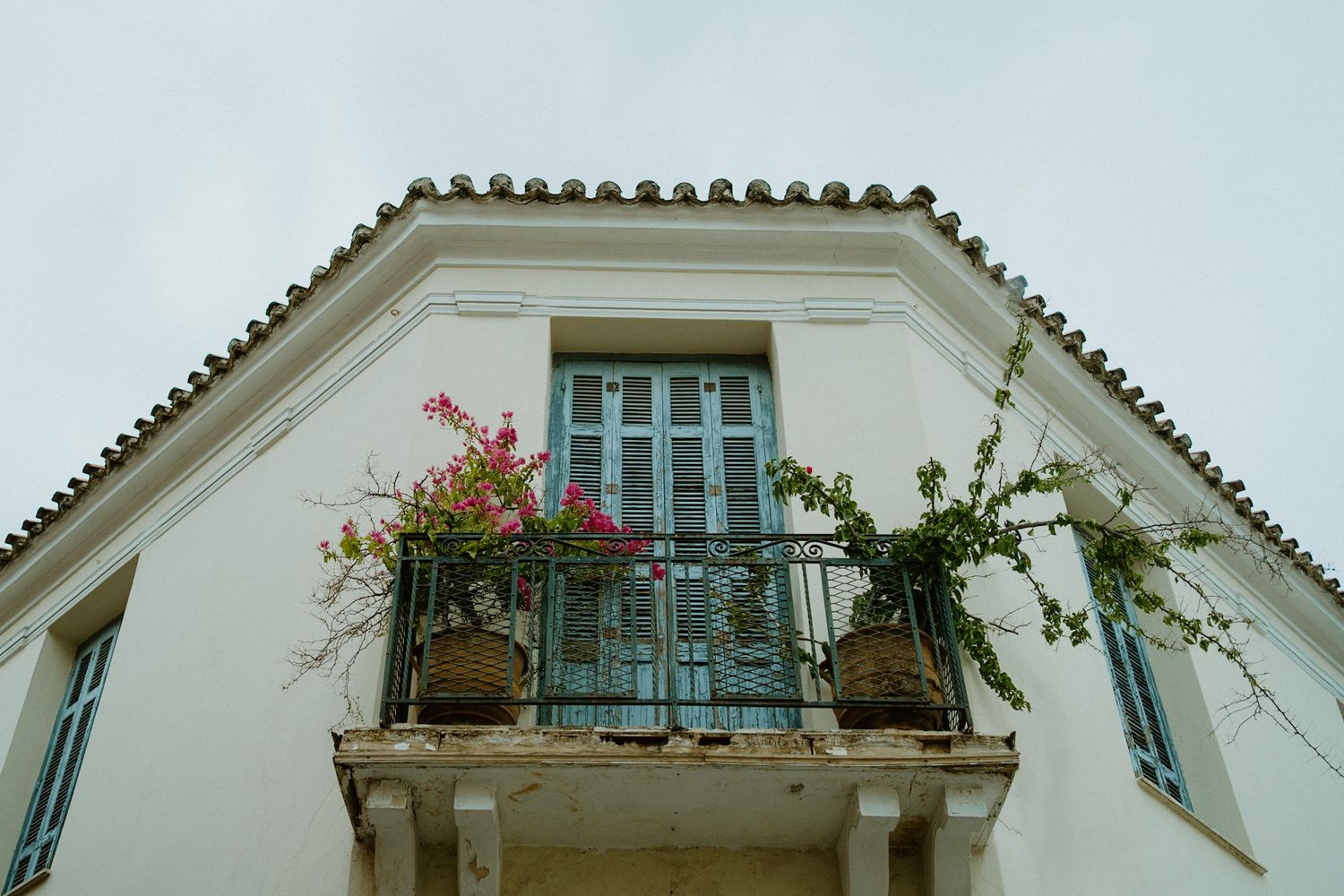 Mediterranean style white building with a decorative balcony adorned with pink and white flowering plants.