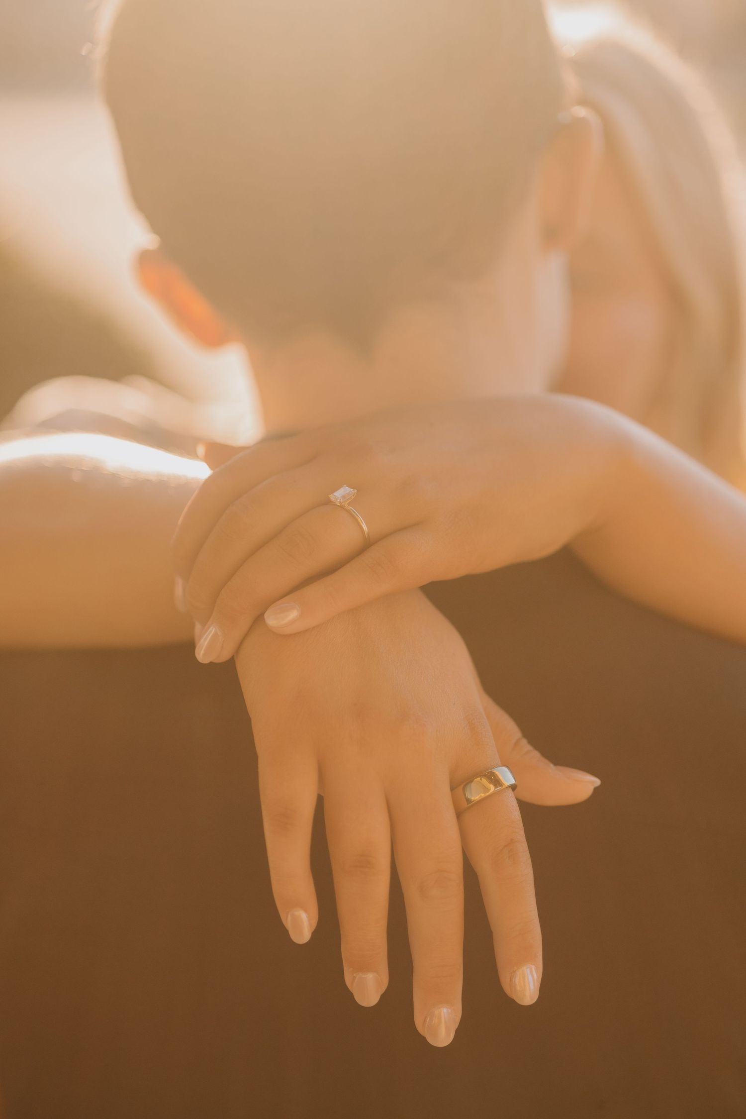 Close up of hands with wedding rings in warm golden light.