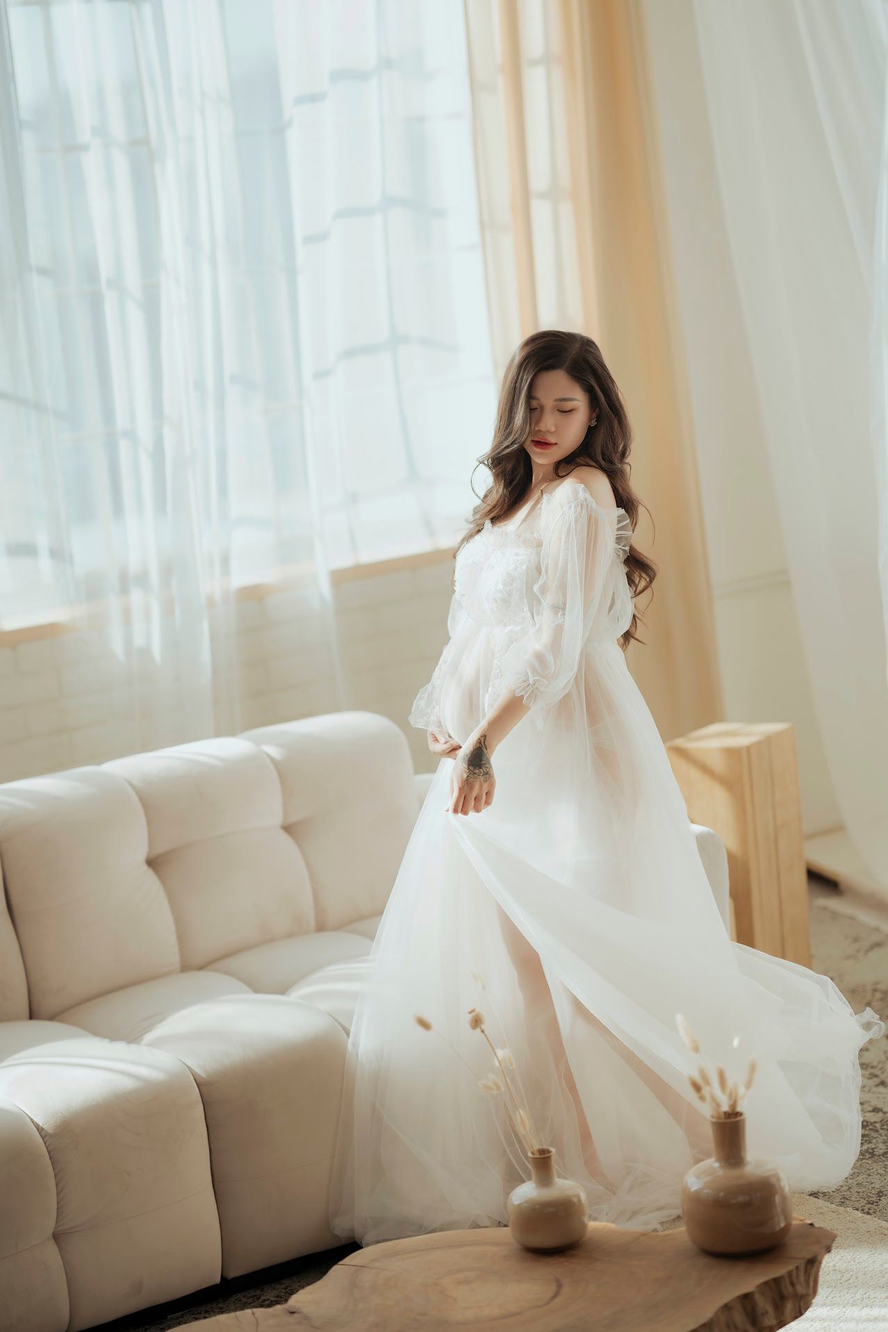 Elegant white flowy dress photographed in bright minimal interior with beige sofa.