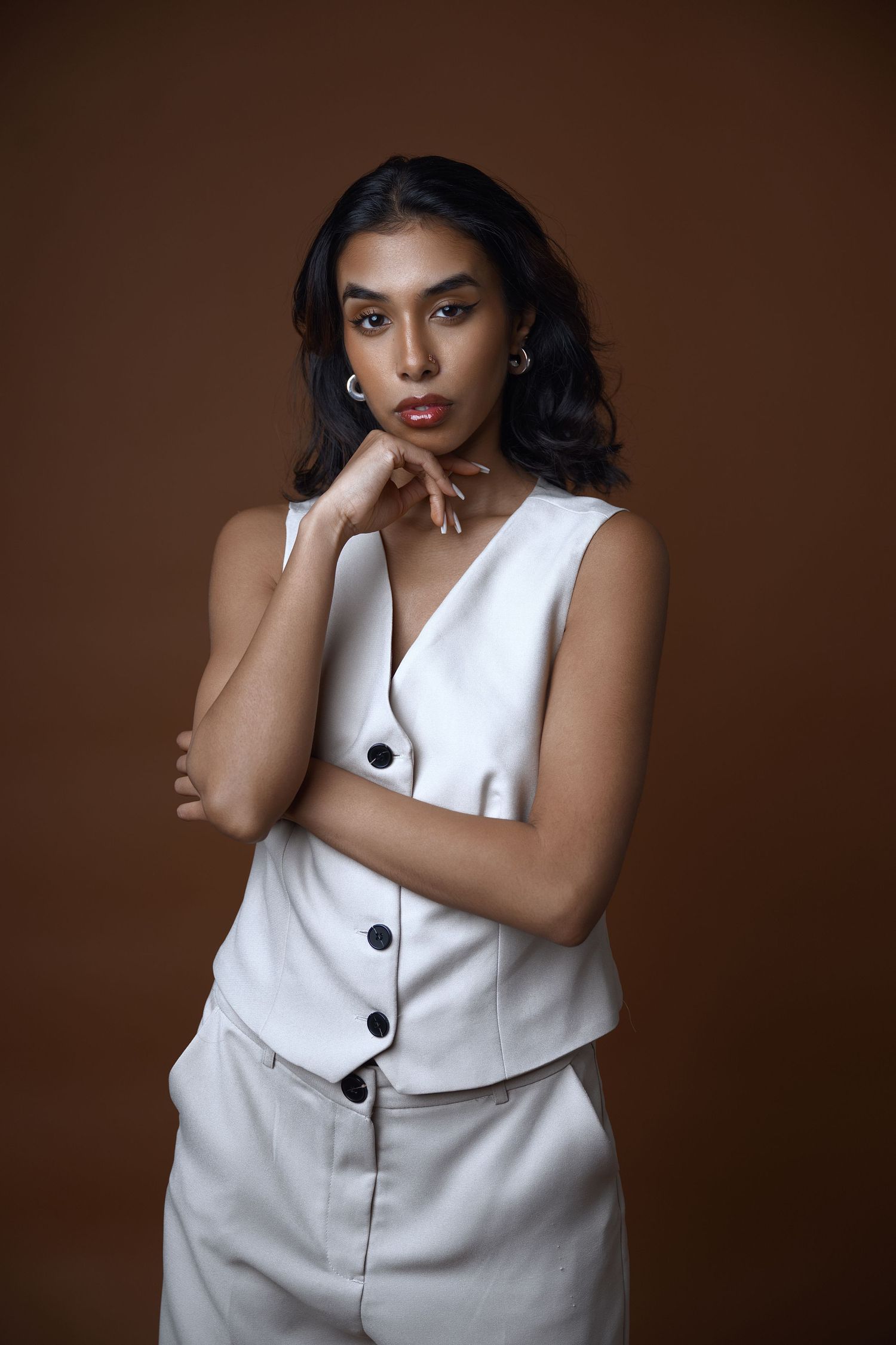 Elegant model in white button-up vest poses against brown backdrop.
