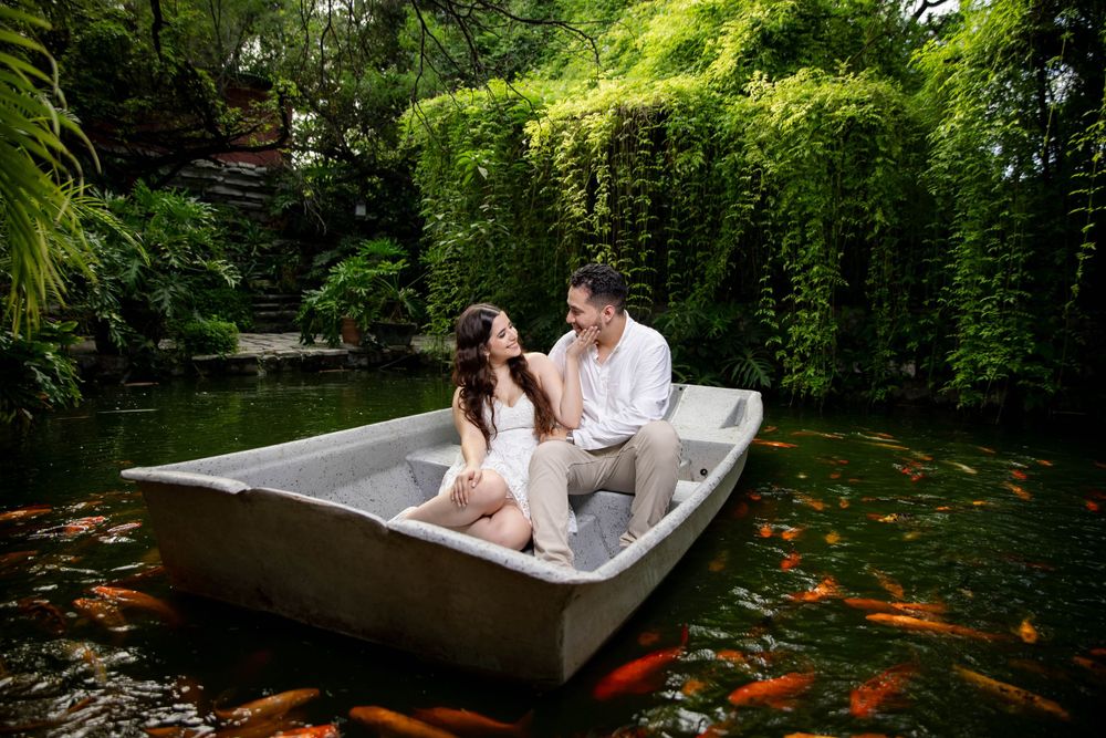 Couple sitting in small boat on pond with koi fish and lush garden backdrop.