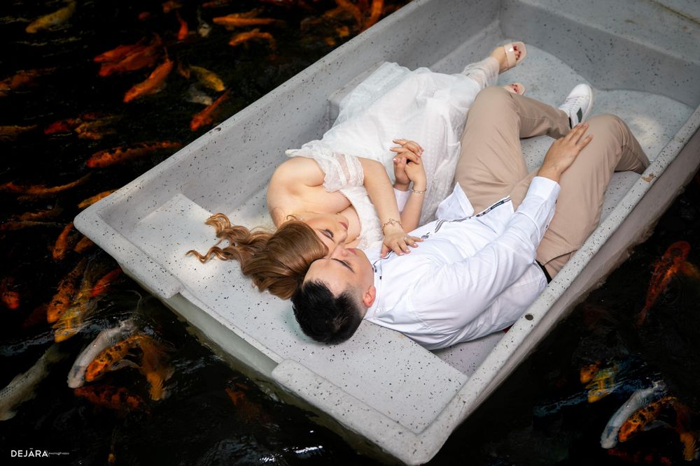 Couple lounges together in gray boat surrounded by koi fish in dramatic lighting.