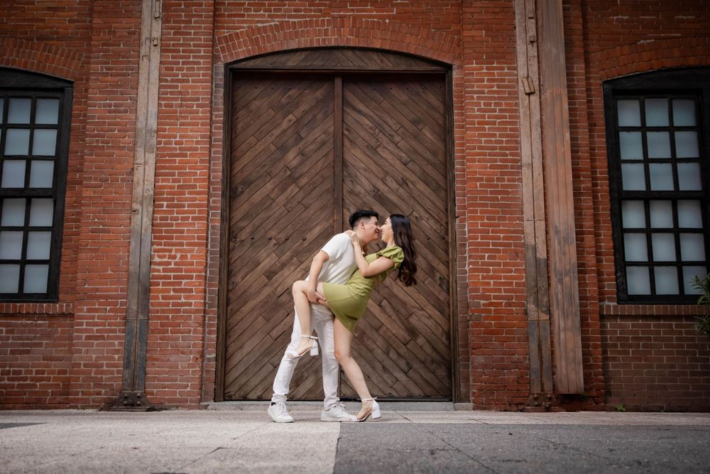 A couple dances romantically in front of a wooden door on a brick building.