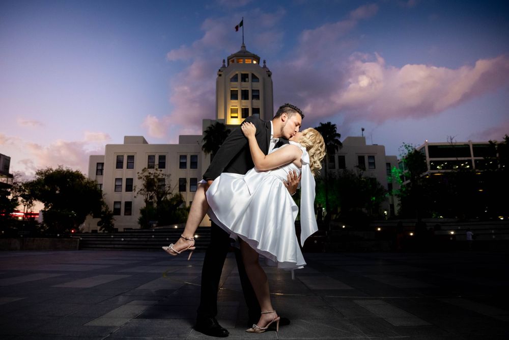 Romantic dip pose in front of a government building at dusk with soft pink clouds.