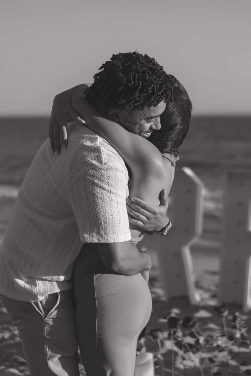 Intimate black and white portrait of couple embracing on beach at sunset.