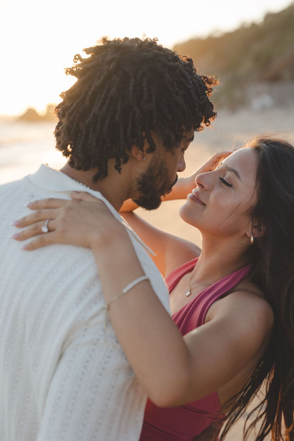 A romantic couple embraces during a sunset photoshoot on the beach, bathed in golden hour light.
